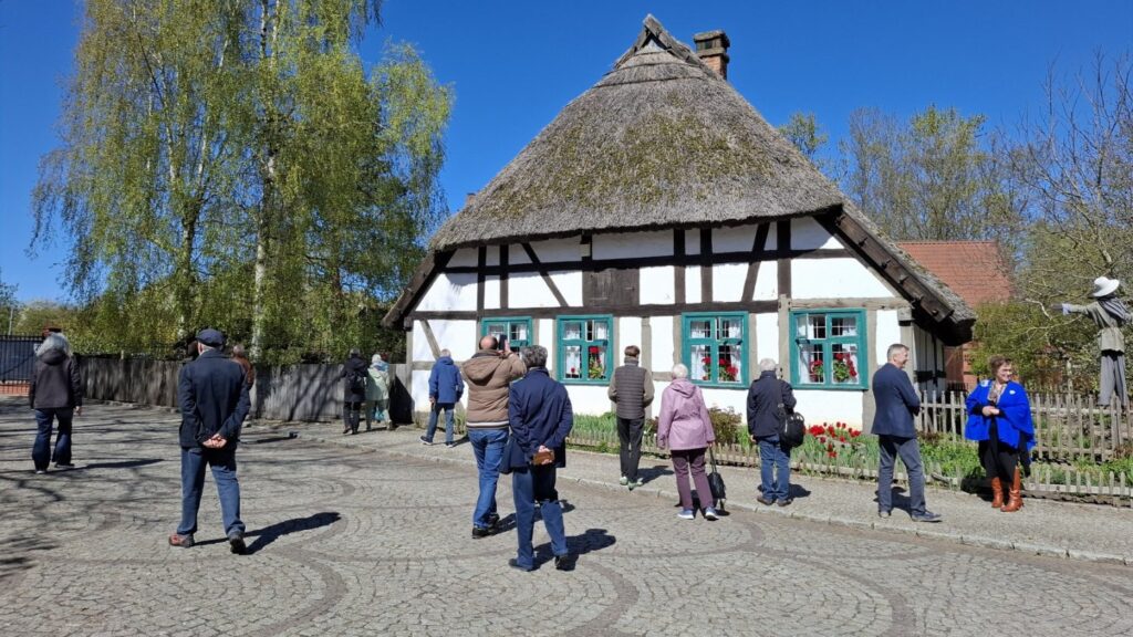 Zwiedzający stoją przed zabytkową chałupą rybaka podczas spaceru (kliknięcie powiększy zdjęcie).
