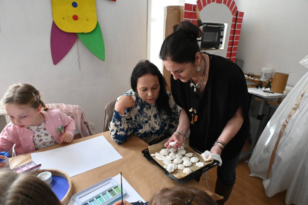 Prowadząca warsztaty pokazuje uczestnikom przygotowane materiały do zajęć plastycznych (kliknięcie powiększy zdjęcie).