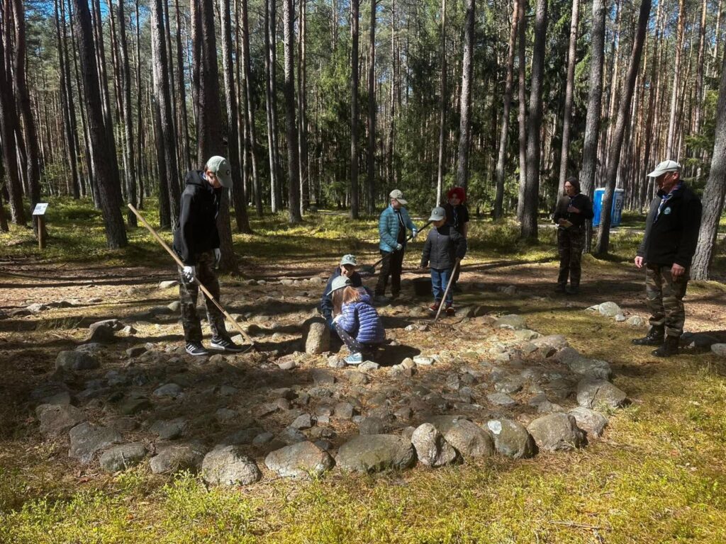 Uczestnicy wspólnie oczyszczają kamienny krąg podczas społecznej akcji porządkowania stanowiska archeologicznego w Grzybnicy (kliknięcie powiększy zdjęcie).