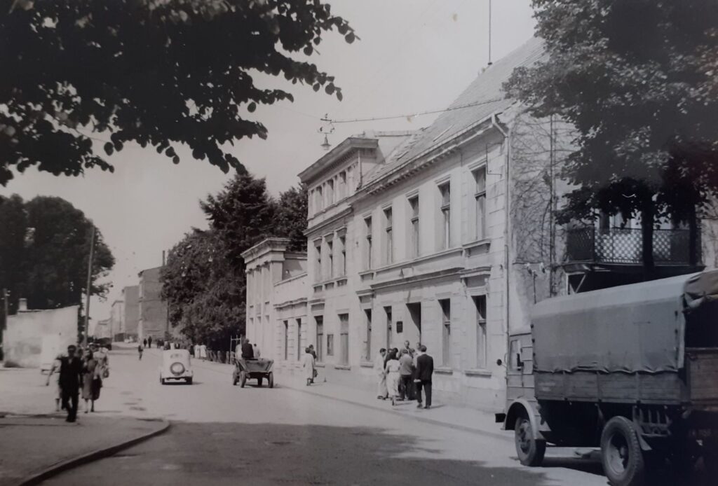 Archiwalne zdjęcie ulicy z reprezentacyjnym budynkiem, pieszymi oraz samochodem ciężarowym zaparkowanym przy jezdni (kliknięcie powiększy zdjęcie)