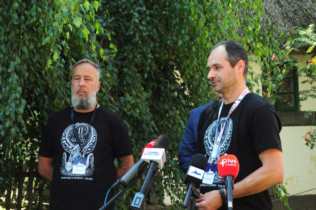 Mężczyzna przemawia podczas konferencji prasowej; przed nim ustawiono mikrofony kilku stacji radiowych i telewizyjnych, a obok stoi drugi uczestnik wydarzenia (kliknięcie powiększy zdjęcie).