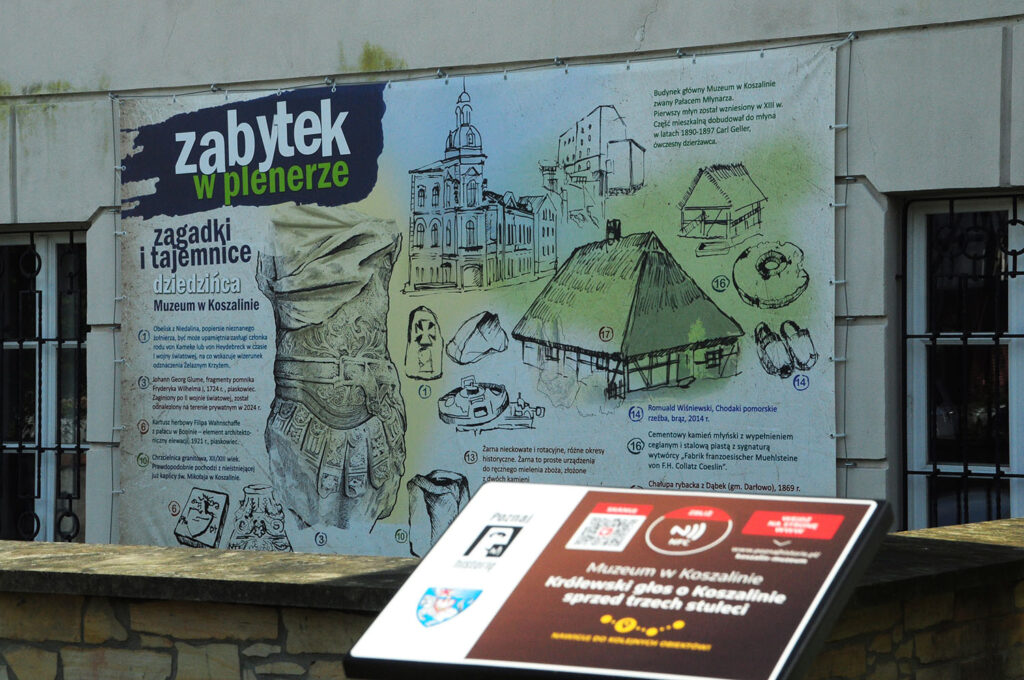 Tablica informacyjna z kodem QR do odsłuchania historii pod tytułem "Królewski głos o Koszalinie sprzed trzech stuleci"; w tle plansza informacyjna wystawy "Zabytek w plenerze", zwieszona na ścianie budynku muzeum (kliknięcie powiększy zdjęcie).